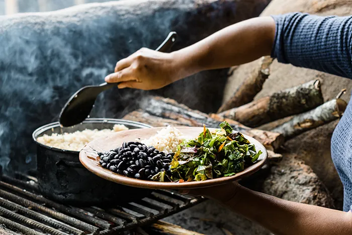 person scooping rice onto plate with beans and salad over an outdoor stove