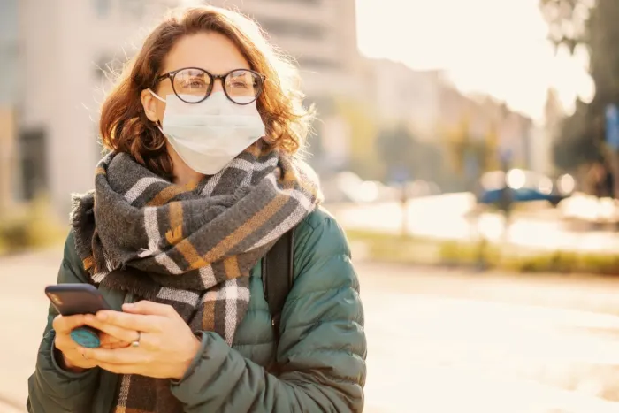 Woman in a protective mask on a city street with a smartphone in her hands
