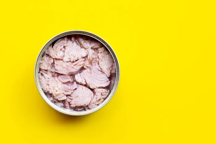 An open can of tuna; flat lay on a yellow surface