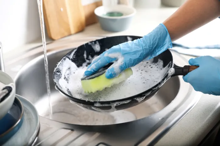 Washing a frying pan with gloved hands and a sponge