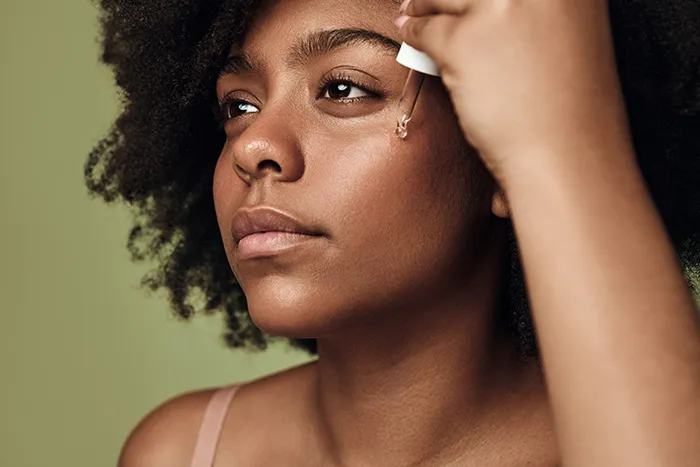 woman using dropper to apply serum to her cheek