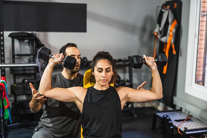 woman lifting free weights with spotter in a gym