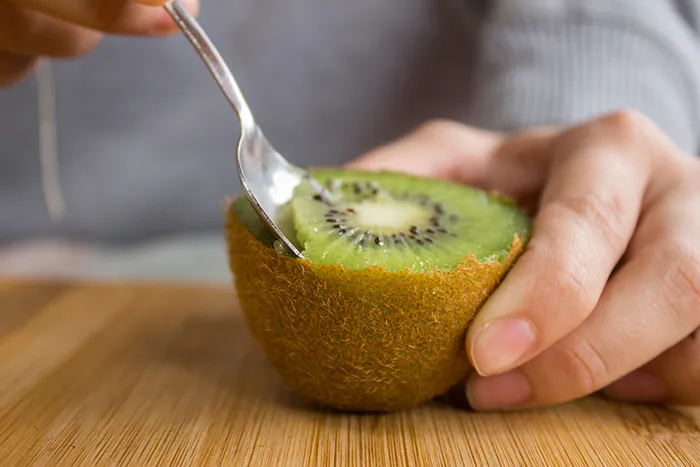 person scooping a half kiwi with a spoon