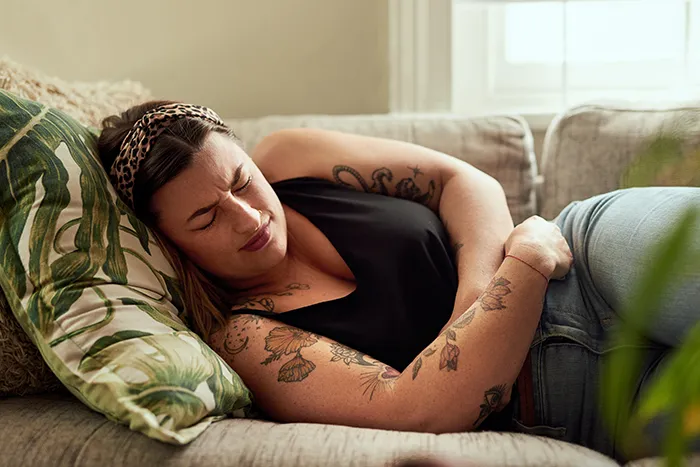woman holding stomach in pain while laying on couch
