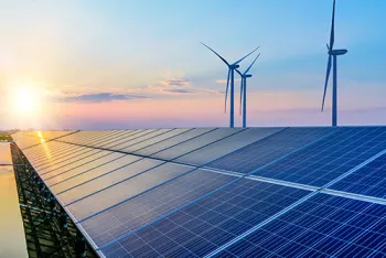 sun shining on solar panels with windmills behind