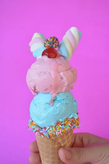 Two scoops of colorful ice cream with sprinkles, candies, and a maraschino cherry