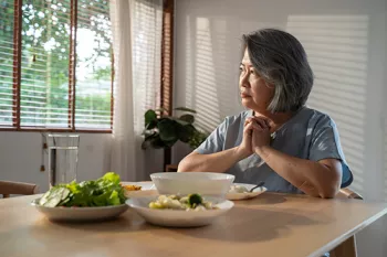 woman looking out a window while sitting at a dining table with food