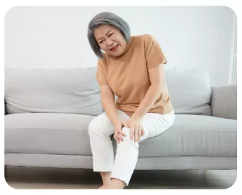 Woman sitting on couch wincing and holding her knee