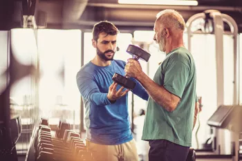 younger mam helping an older man weight lift
