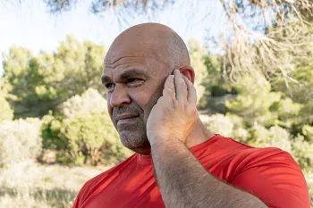 man outside holding his ear seeming to be in pain