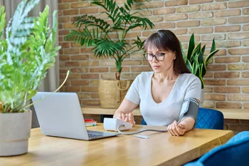 woman checking her blood pressure sitting at a dining table.