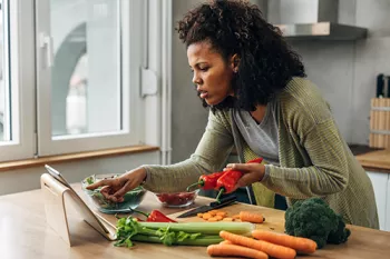 woman checking ipad while cutting vegetables in kitchen