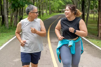 Man and woman running on a paved trail in a tree lined park