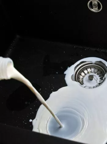Milk being poured into a black sink; food waste due to date label confusion