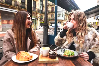 2 women eating and drinking coffee outside at a cafe