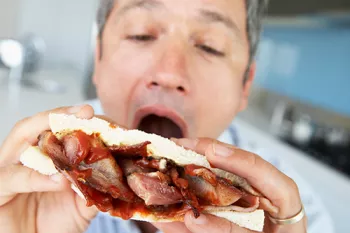man taking a bite out of a sandwich full of red meat and barbeque sauce
