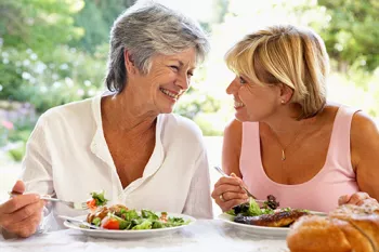 2 women eating salads outside and looking at eachother