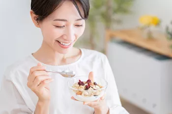 woman eating a small yogurt parfait out of a clear bowl
