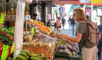 woman wearing backpack looking a produce in outdoor market