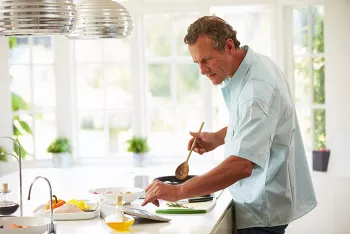 man cooking in bright kitchen with bottle of oil on the counter