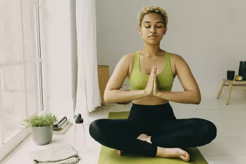 woman in green top sitting crisscross on green yoga mat with prayer hands and eyes closed