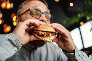 man wearing glasses taking a bite of a cheese burger