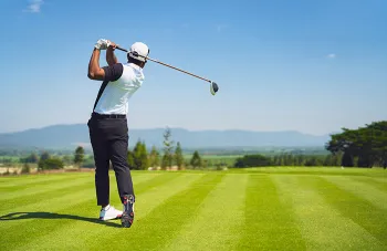 man swinging golf club on green grass