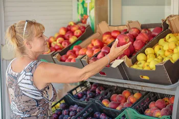 woman picking out fruit from wooden boxes