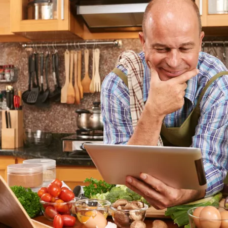 man in kitchen looking at ipad with lots of vegetables on the counter