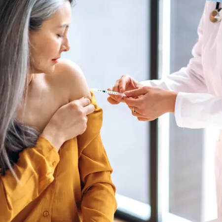 women in yellow top receiving a vaccine from the doctor