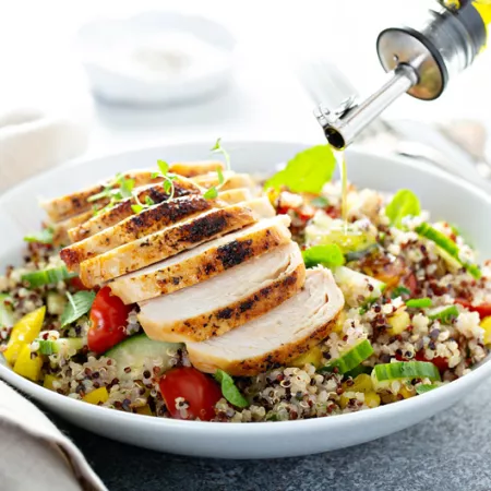 bowl of salad topped with chicken with olive oil drizzled on top