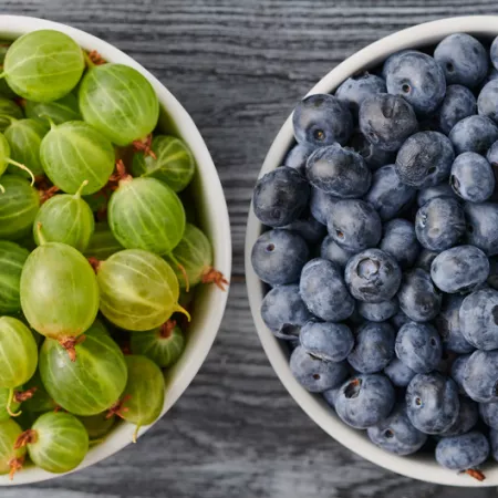 a bowl of gooseberries on the left and bowl of blueberries on the right