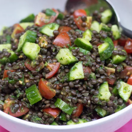 White bowl filled with black lentils, chopped cucumbers and tomatoes