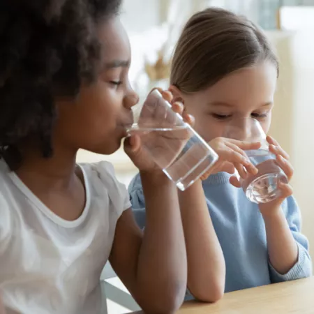 2 young girls drinking water out of clear glasses