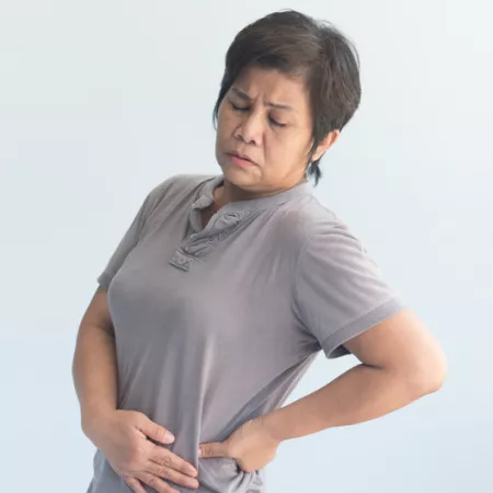 woman in grey shirt holding her hip and wincing in pain