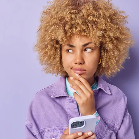 person in purple shirt with purple background holding a phone and holding their chin