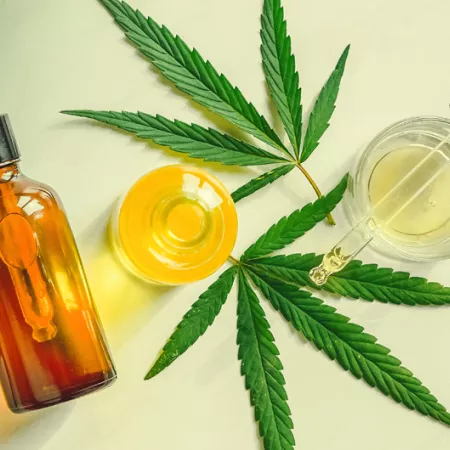 flat lay of marijuana leaves and oils in clear bottles