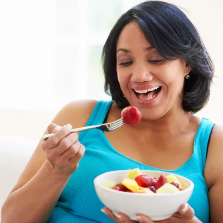 woman eating a bowl of cut fruit