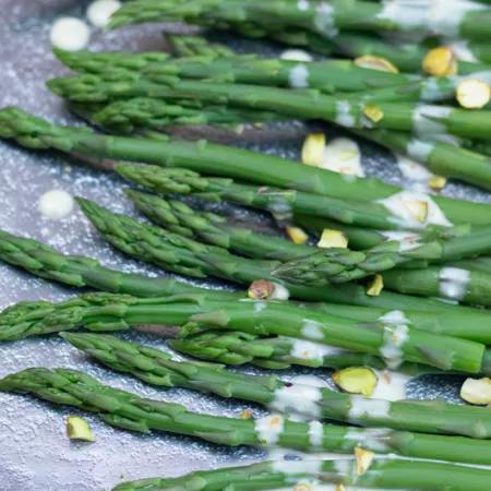 cooked asparagus covered in sauce and pistachios