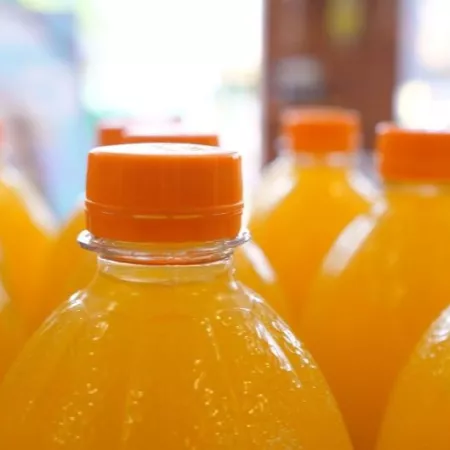 Close up of top parts of orange soda in plastic bottles on a display in a supermarket