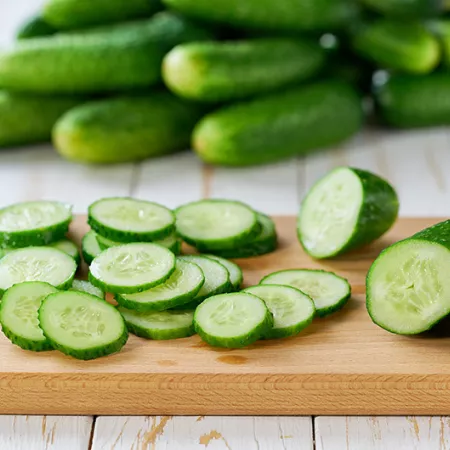 Whole and sliced fresh cucumbers on a cutting board on a wooden table