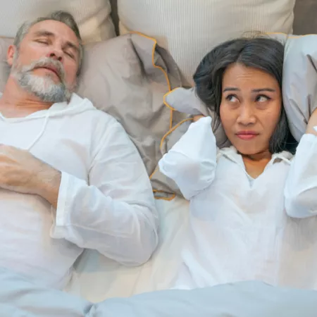 one person sleeping soundly and the person next to them shielding their ears with a pillow