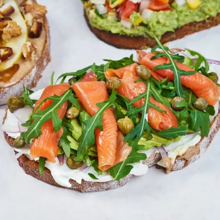Slices of toast topped with salmon, nuts, and avocado, respectively.