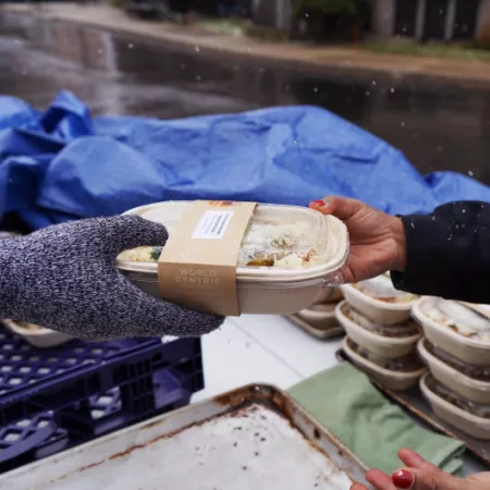 A Make Food Not Waste worker hands a recipient a meal