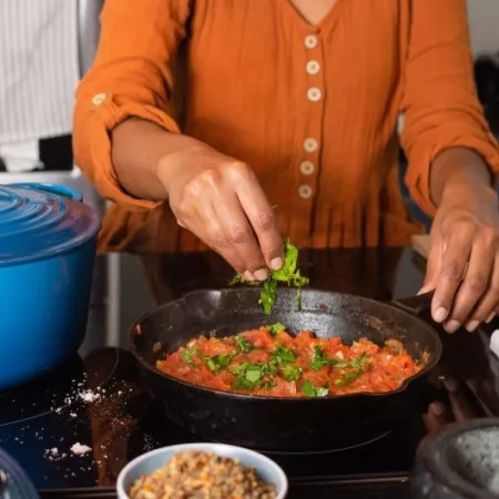 A woman in an orange shirt tears basil over a pot of tomato sauce