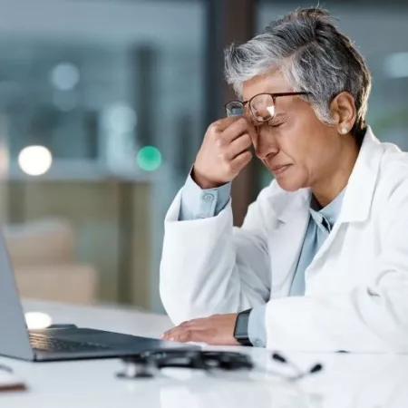 Doctor experiences headache while reviewing data on a laptop