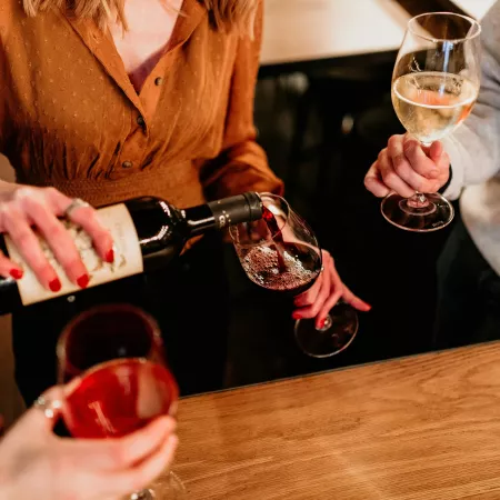 A seated woman pouring herself a glass of red wine.