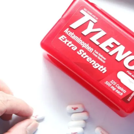A hand picks up a tablet of Tylenol from a white surface beside a red bottle of Tylenol Extra Strength acetaminophen, which RFK and Trump wrongly assert causes autism.