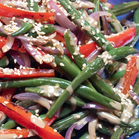 green beans and sliced peppers covered in sauce and sesame seeds