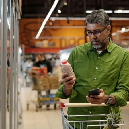 A man ina  green shirt reads the label on a packaged food product in a grocery store